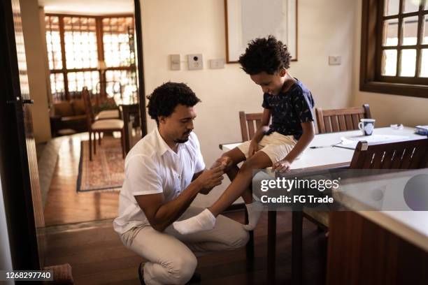 pai cuidando do filho com o joelho machucado em casa - knees together - fotografias e filmes do acervo