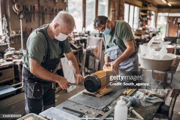 senior men with protective face masks rebuilding an engine in workshop - small business mask stock pictures, royalty-free photos & images