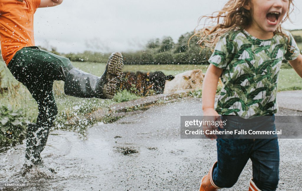 Two children in welly boots play in a Huge Puddle