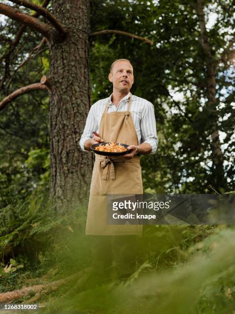 man male chef outdoors with chanterelles mushrooms and frying pan - cooked mushrooms stock pictures, royalty-free photos & images
