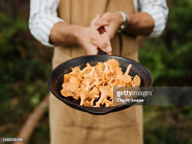 man male chef outdoors with chanterelles mushrooms and frying pan - cooked mushrooms stock pictures, royalty-free photos & images