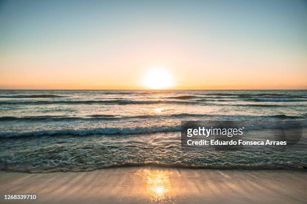 sunrise over a tranquil caribbean sea, waves receding at the beach, against a clear sunny blue sky - 水平線 ストックフォトと画像