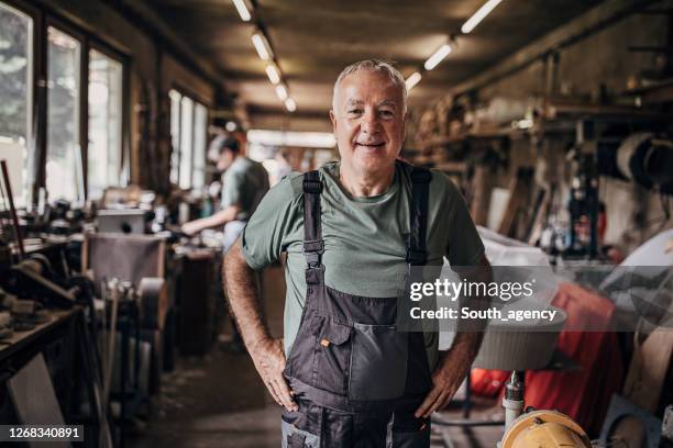 portrait of a senior man who is standing in workshop - empreiteiro de reparações imagens e fotografias de stock