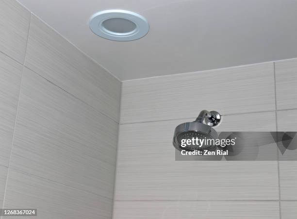 shower head on a bathroom ceramic tile wall and circular light fixture on the ceiling - bathroom ceiling stock pictures, royalty-free photos & images