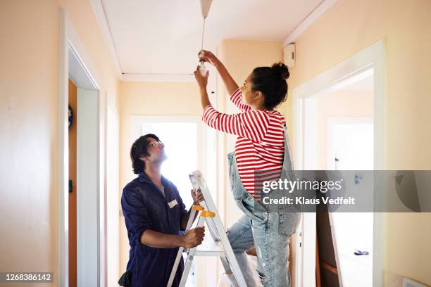 couple changing light bulb while renovating home - step ladder stock pictures, royalty-free photos & images
