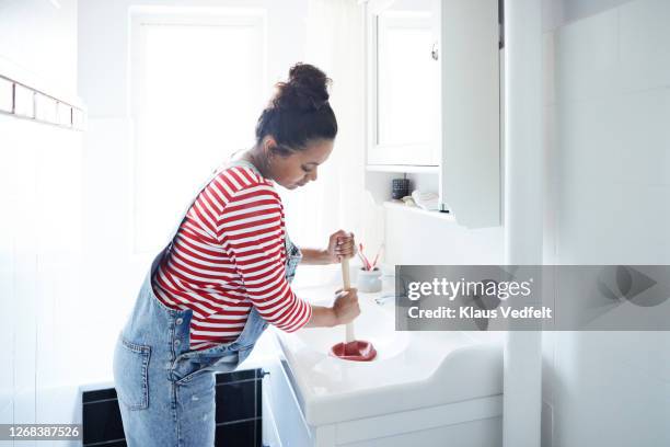 woman unclogging sink with plunger in bathroom - plugging in stockfoto's en -beelden