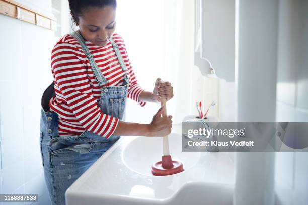 woman plunging clogged sink in bathroom - fontein stockfoto's en -beelden