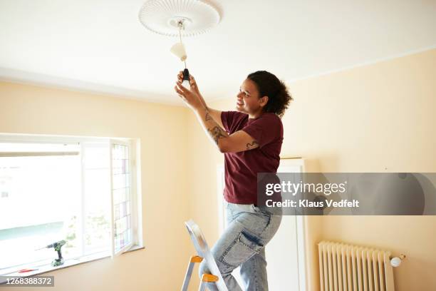 woman changing light bulb at home - installing ceiling light fixture stock pictures, royalty-free photos & images