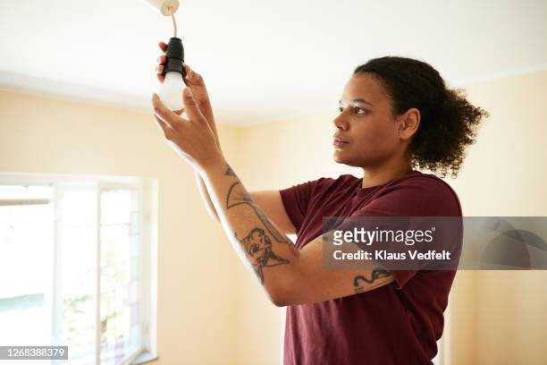 woman changing light bulb in living room - autarkie stockfoto's en -beelden