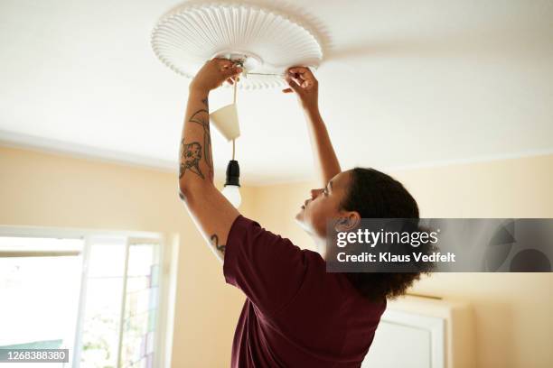 woman connecting light bulb on ceiling at home - luz colgante fotografías e im�ágenes de stock