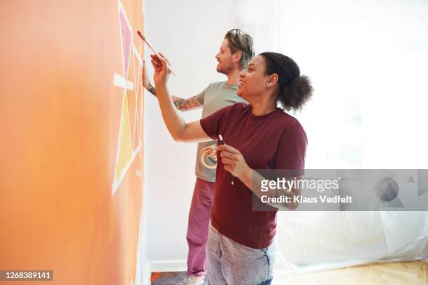 couple painting design on orange wall at home - couple painting stock pictures, royalty-free photos & images