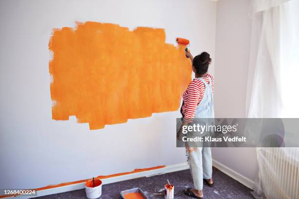 woman painting wall while renovating home - naranja color fotografías e imágenes de stock