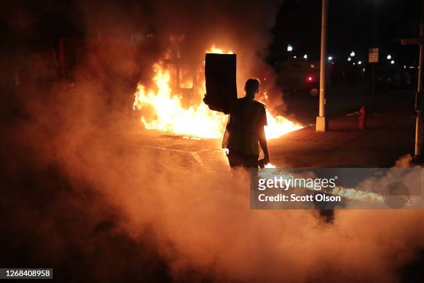 Leaking diesel fuel from a burning garbage truck leaves a trail of fire in front of a protester during a second night of rioting on August 24, 2020...