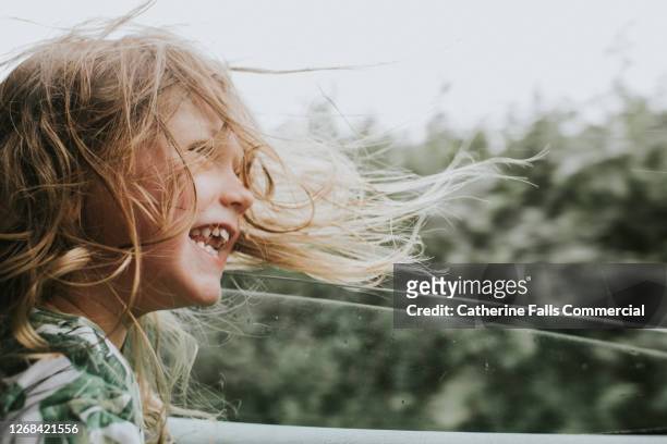 happy little girl beside an open car window as her hair blows in the wind - fenster stock-fotos und bilder