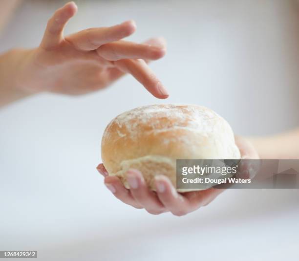 woman holding and about to press finger into soft white bread roll, close up. - bun 個照片及圖片檔