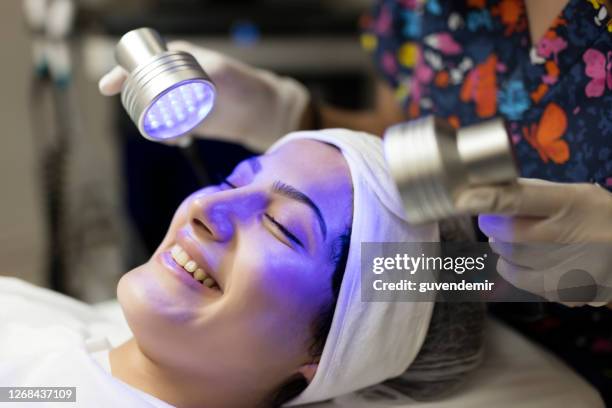 female beautician doing blue light therapy on face of pretty young woman - laser face stock pictures, royalty-free photos & images