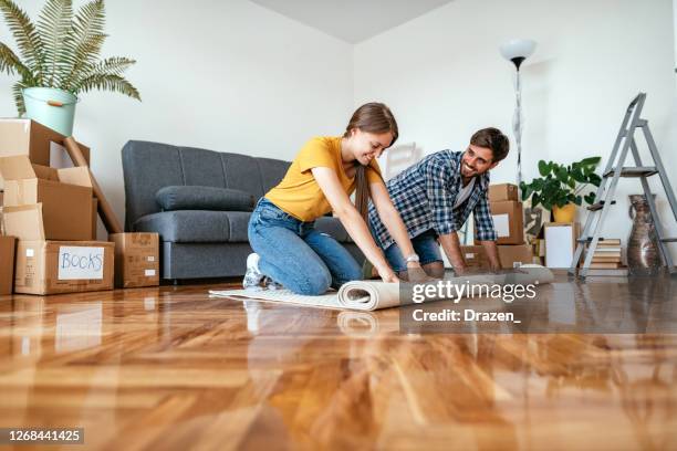 paar zieht in neue wohnung. mann und frau rollen den neuen teppich auf dem boden in neue wohnung - carpet roll stock-fotos und bilder