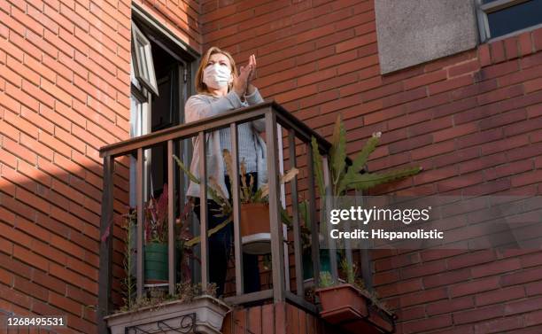 woman applauding doctors and nurses from her balcony wearing a facemask - applauding nurses stock pictures, royalty-free photos & images