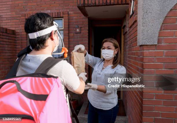 woman receiving a delivery order at home while wearing a facemask - biosecurity stock pictures, royalty-free photos & images