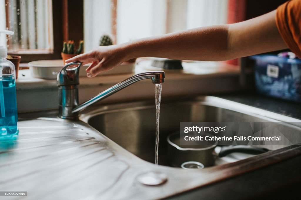 Hand turning off a Running Chrome Tap in a kitchen