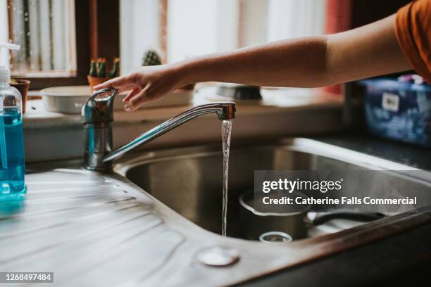 hand turning off a running chrome tap in a kitchen - vattenhushållning bildbanksfoton och bilder