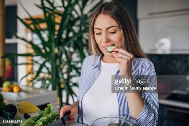 ビーガンサラダを準備し、キュウリを味わう台所の女性 - cucumber ストックフォトと画像