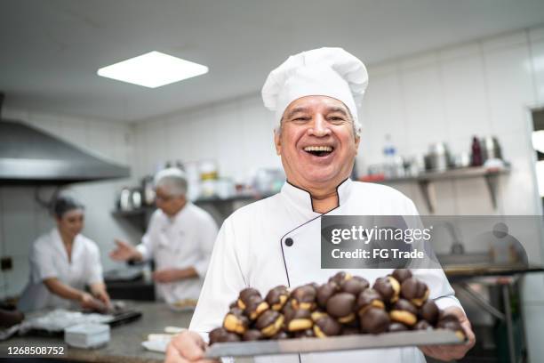 feliz chef senior llevando una bandeja llena de eclairs - pasteleros fotografías e imágenes de stock