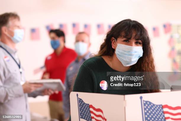 young adult, latin descent woman votes in usa election wearing mask. - voting mask stock pictures, royalty-free photos & images