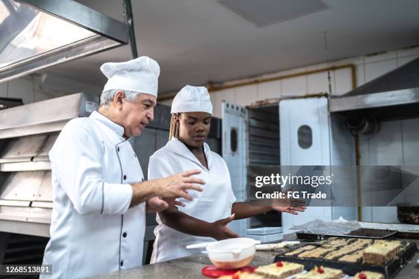 senior chef explaining something to an assistant - pasteleiro imagens e fotografias de stock