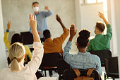 Back view of group of students raising their arms during a class at lecture hall.