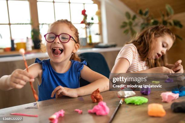 two girls playing with child's play clay while sitting at table at home - child's play clay stock pictures, royalty-free photos & images