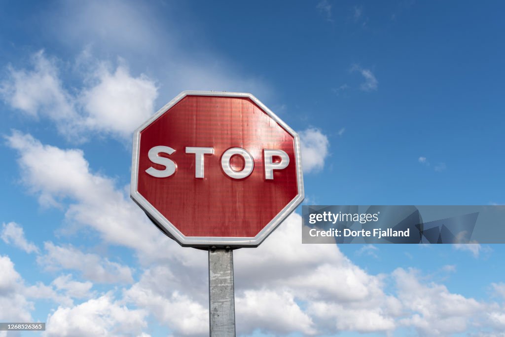 Red stop traffic sign against a blue and white sky