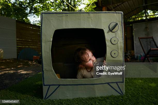 a baby sitting in a cardboard tv looking out. - insight tv stock pictures, royalty-free photos & images