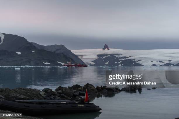 Beginning of the sunset reflected in the Nunatak Needle with detail of the Polar Ship Ary Rongel at anchor in Admiralty Bay on January 10, 2020 in...