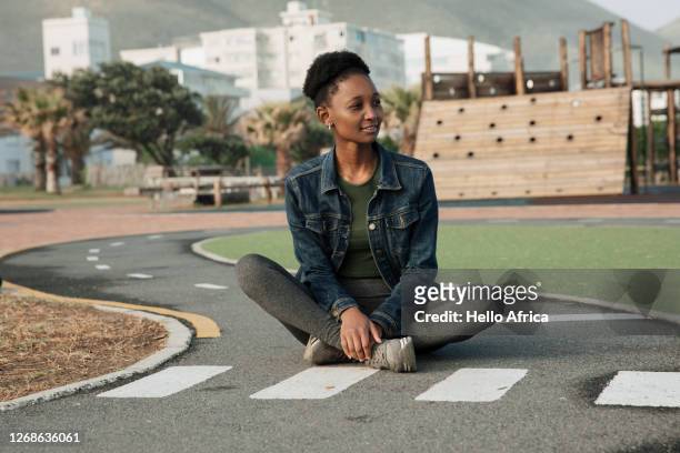 beautiful young woman sitting patiently at a miniature pedestrian crossing - cross legged stock pictures, royalty-free photos & images