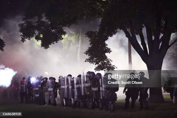 As tear gas fills the air, police try to push back demonstrators near the Kenosha County Courthouse during a third night of unrest on August 25, 2020...