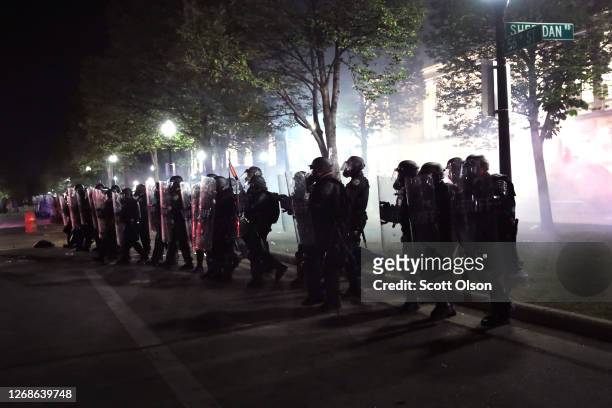 As tear gas fills the air, police try to push back demonstrators near the Kenosha County Courthouse during a third night of unrest on August 25, 2020...