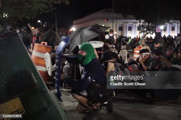 Protesters take cover behind a dumpster as they confront police in front of the Kenosha County Courthouse during a third night of unrest on August...