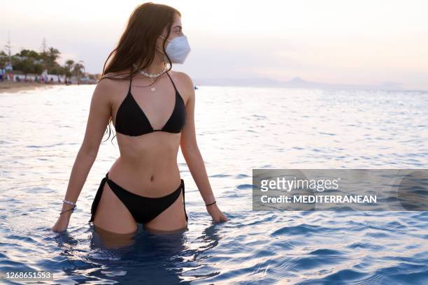 bikini tourist girl on the beach in a pandemic face mask at sunset - swimsuit models girls stock pictures, royalty-free photos & images