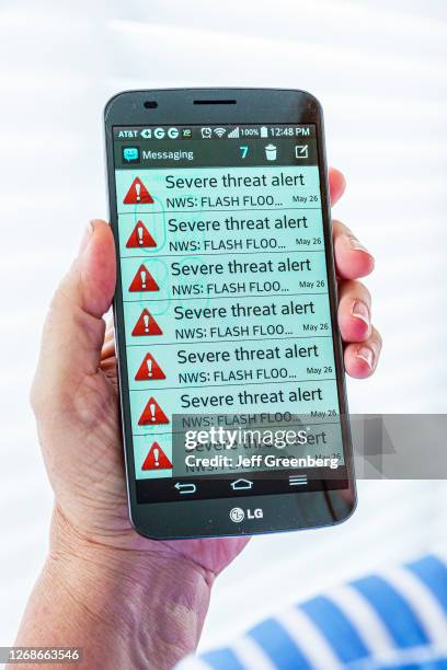 Hand holding smartphone, LG model with severe weather threat, emergency alert message.