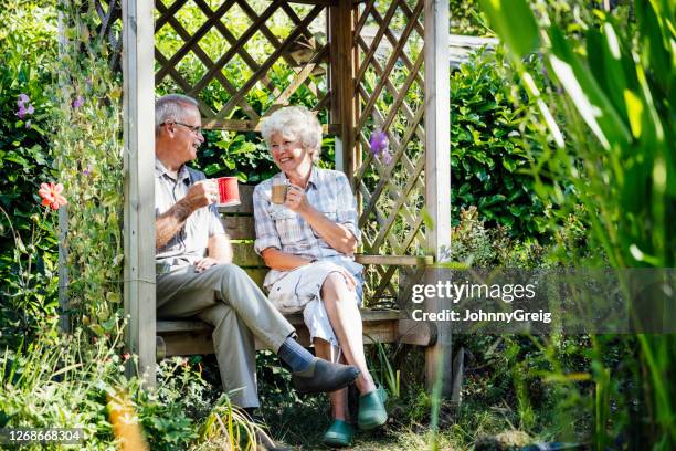 senior-paar genießen kaffee auf der bank im englischen garten - pavillon stock-fotos und bilder