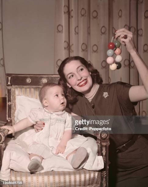 Irish born actress Valerie Hobson shakes a rattle to amuse her baby son Mark Havelock-Allan at home in England in 1951.