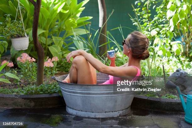 woman bathing in small tin tub in the garden, enjoying a cup of coffee - cooling down stockfoto's en -beelden