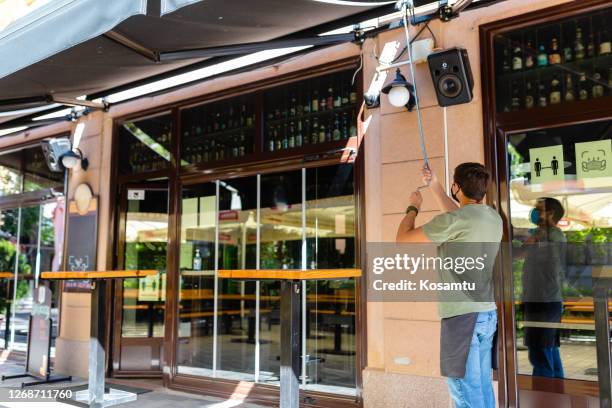 waiter adjusting awning in front of his pub to make a shade for customers - awning stock pictures, royalty-free photos & images