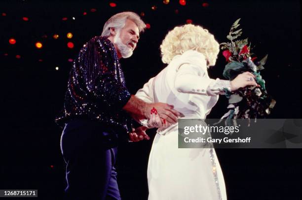 American Country musician Kenny Rogers escorts Dolly Parton, who holds a bouquet of red roses, as they walk offstage during a performance at Nassau...