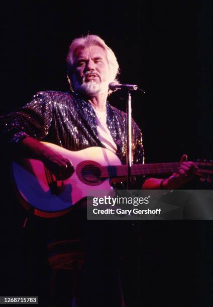 American Country musician Kenny Rogers plays guitar as he performs onstage at Nassau Coliseum, Uniondale, New York, August 29, 1985.