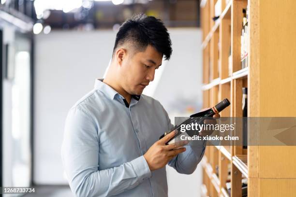 a man is looking at a bottle of red wine - choosing wine stock pictures, royalty-free photos & images