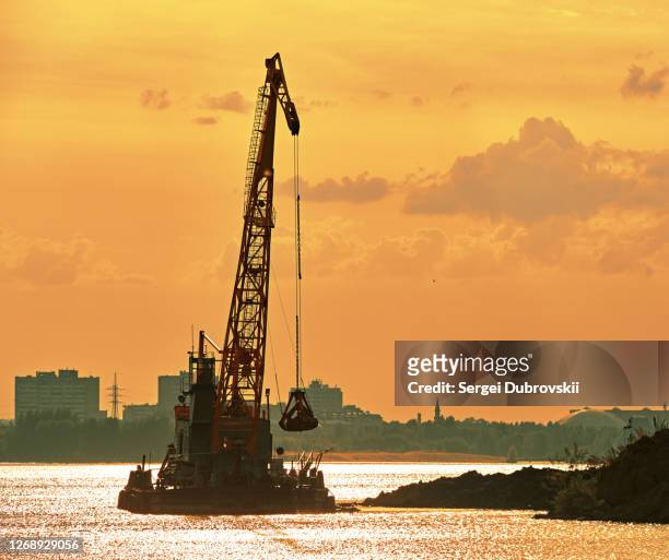 dredging crane working near shore, back evening orange sunlight reflection - dredger stock pictures, royalty-free photos & images