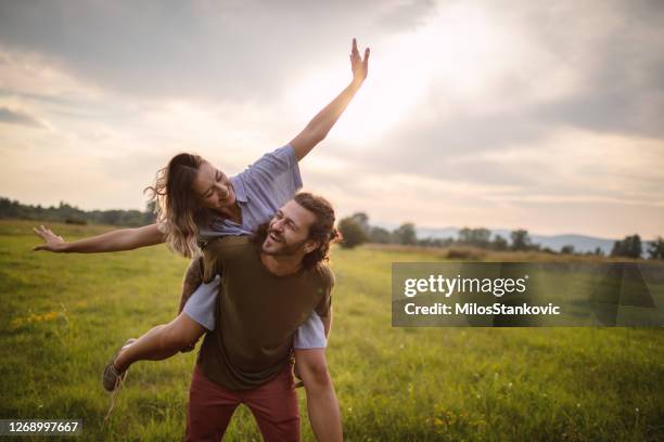 liebespaar auf einer wiese - person auf den schultern tragen stock-fotos und bilder