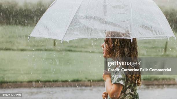 mesmerised little girl holds a transparent umbrella in a heavy rainstorm - umbrella protection stock pictures, royalty-free photos & images